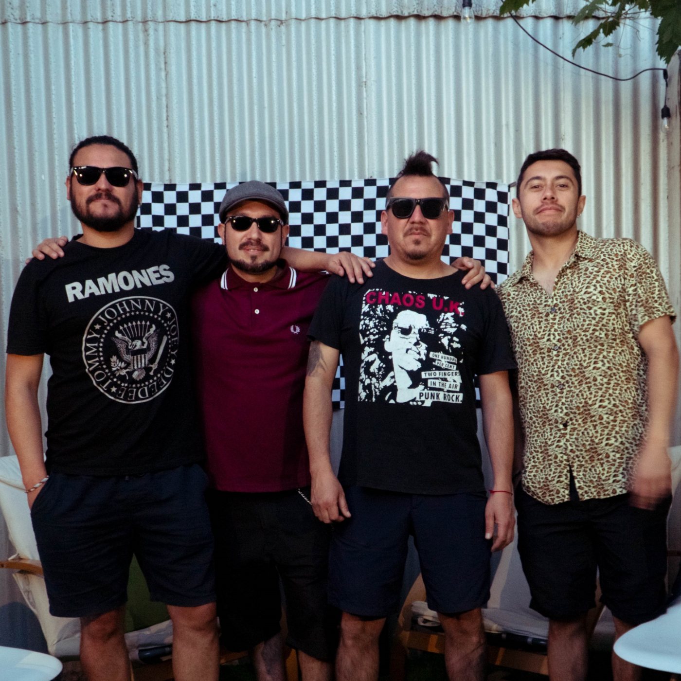 Los cuatro integrantes de Spinazo Ska de pie, con un damero blanco y negro detrás.