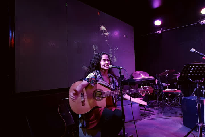 Fiorela Giraldo cantando con guitarra bajo las luces del escenario.